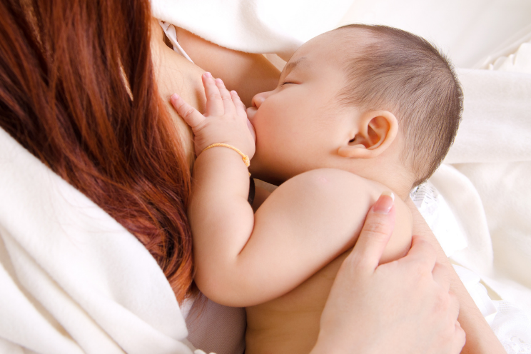 red haired woman breastfeeding a sleepy baby