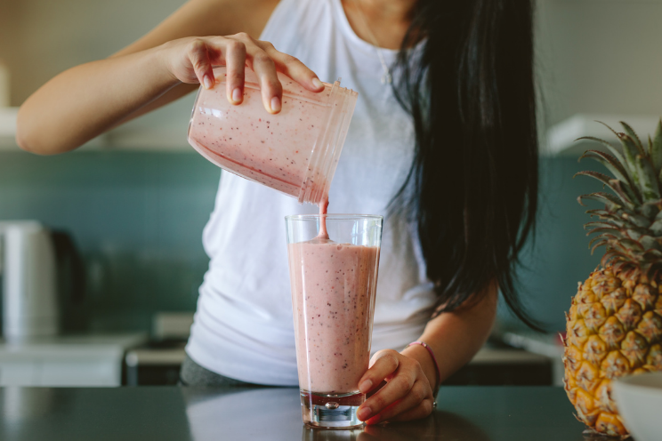 dark haired woman pouring a lactation smoothie into a glass